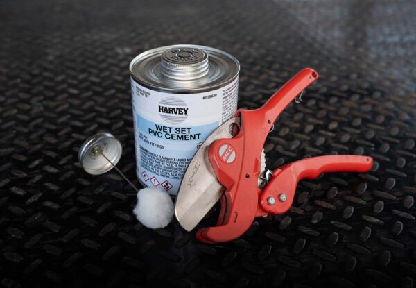 PVC pipe cement and red pipe cutter tools used for irrigation system installation